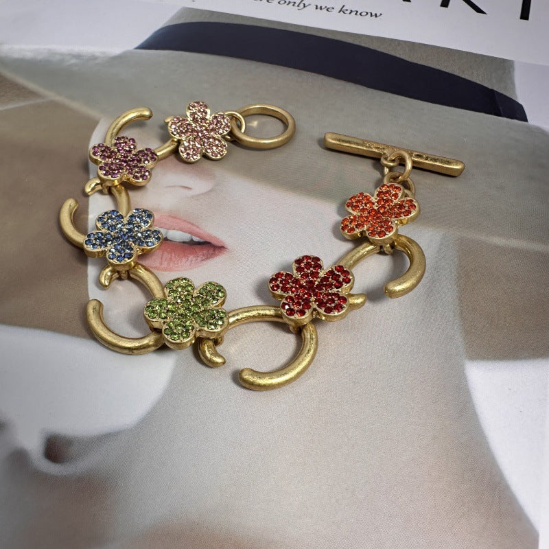 Buntes Blumenarmband mit goldfarbenen Gliedern und funkelnden Steinen in Plomme-Optik