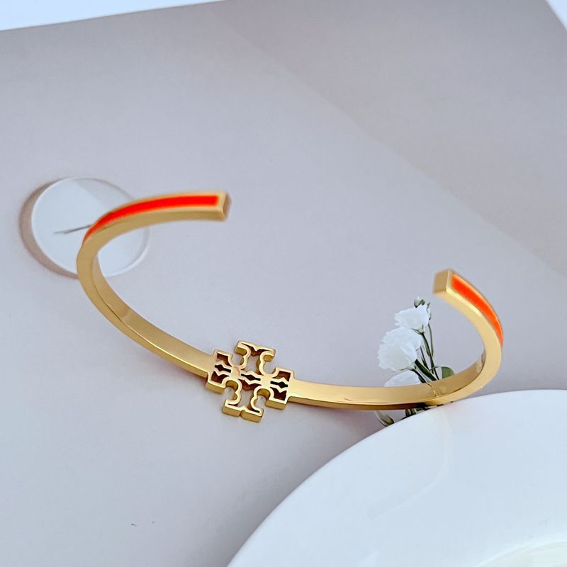 Gold open metal bangle with cutout logo and orange-red enamel trim stripe