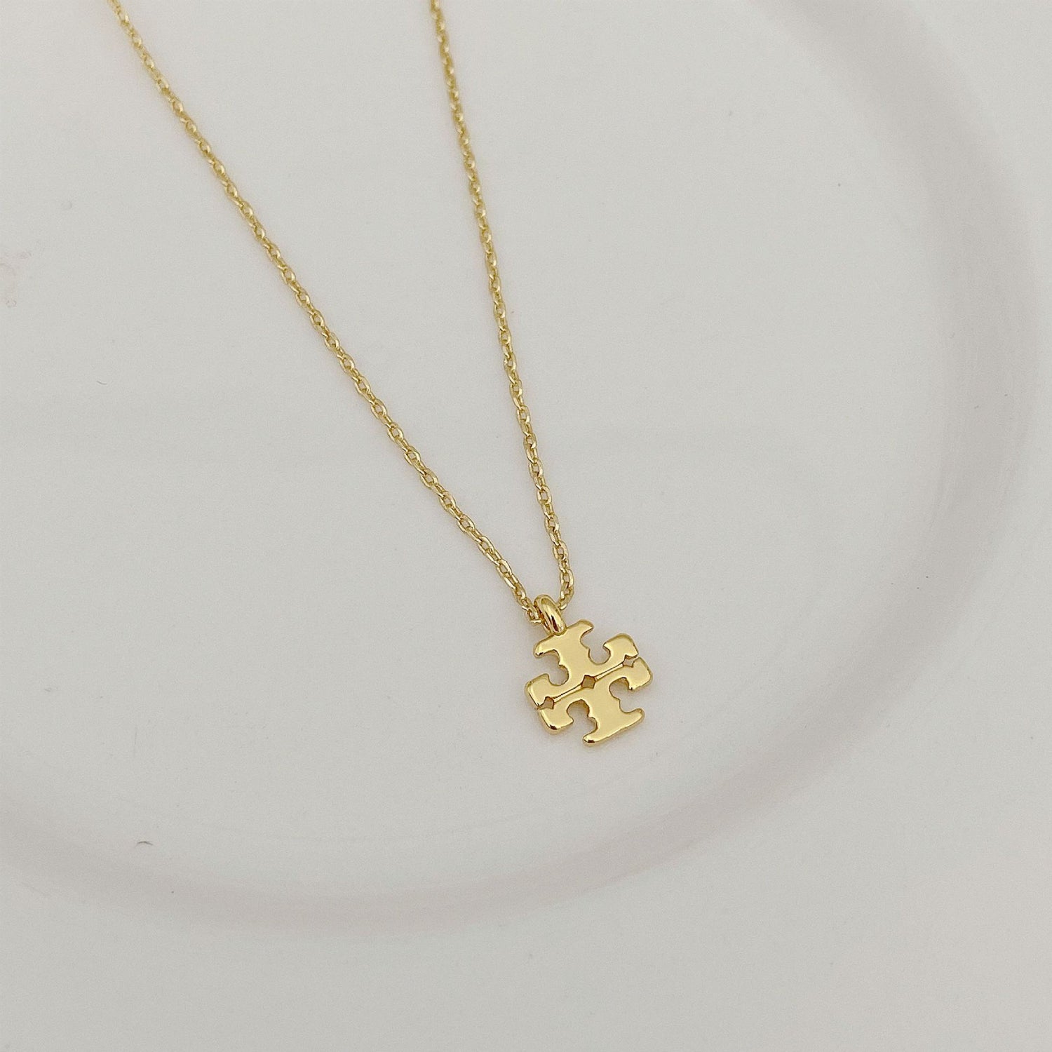 Gold logo pendant necklace with small jigsaw-style charm on thin chain