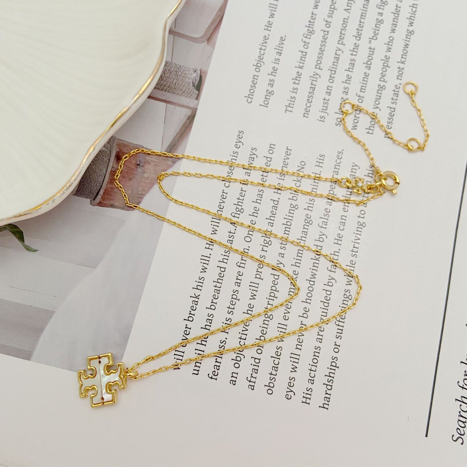 Gold-tone pendant necklace with logo charms and linked chain, shown on book