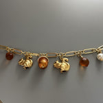 Gold-tone bracelet charm row with squirrel, pinecone, acorn and brown beads, pearl detail