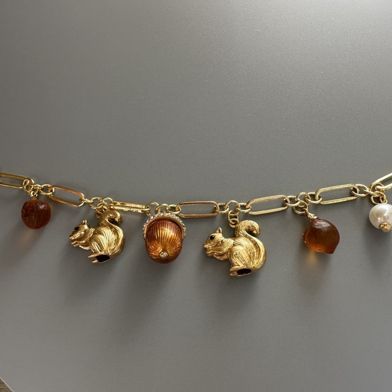 Gold plated charm bracelet close-up: squirrel and acorn charms with amber beads and faux pearls.