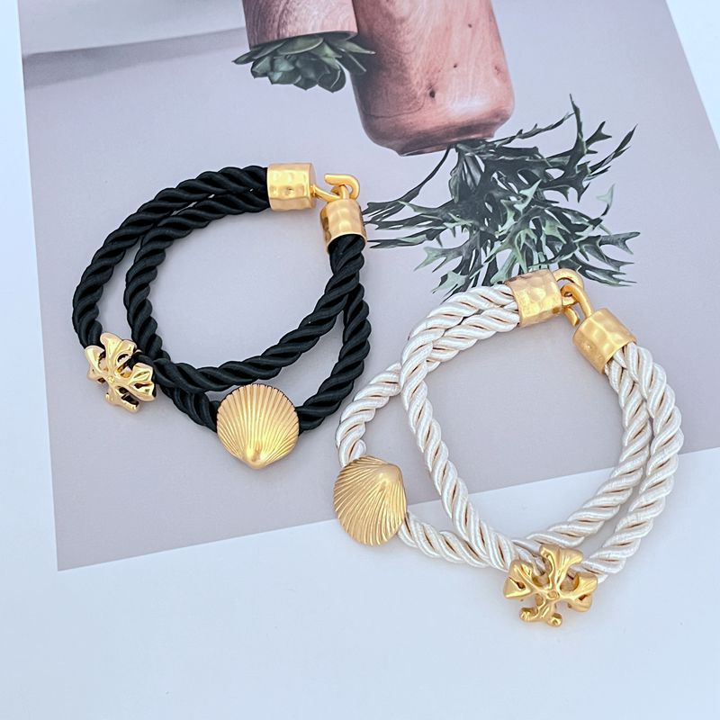 Two braided cord bracelets, black and white cords with gold clasp and shell charms.