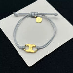 Ajustable pulsera con cordón gris y dijes esmaltados dorados, cierre con botón amarillo