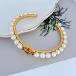 Gold-tone open bangle with white pearl row and centered logo detail