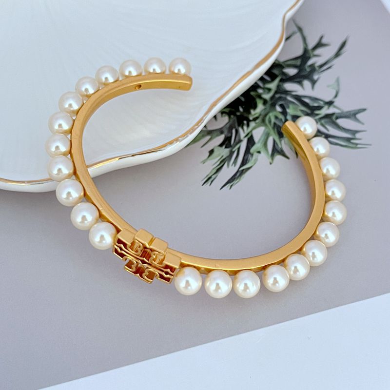Gold-tone open bangle with white pearl row and centered logo detail
