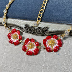 Close-up enamel cherry blossom pendant necklace with red flowers and gold filigree center
