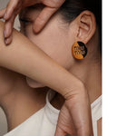 Gold round metal stud earrings with miu miu logo on ear