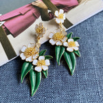 White enamel floral drop earrings with gold bead flowers and green leaf accents