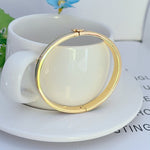 Gold-tone hinged bracelet with small clasp at top, smooth round bangle profile