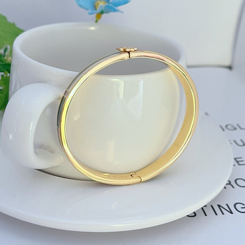 Gold-tone hinged bracelet with small clasp at top, smooth round bangle profile