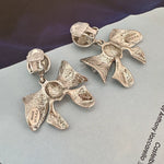Silver-tone bow drop earrings with clip backs and textured ribbon bows