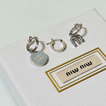 Three-piece enamel hoop earrings with light blue round charm and silver-tone metal hoops