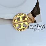 Gold circular openwork logo hair clip with smooth metal rim and twin prongs