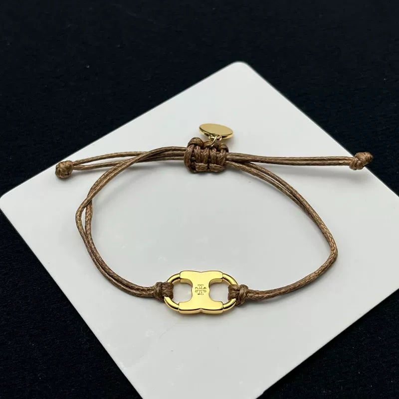 Brown woven adjustable drawstring bracelet with gold clover enamel charm and small round tag