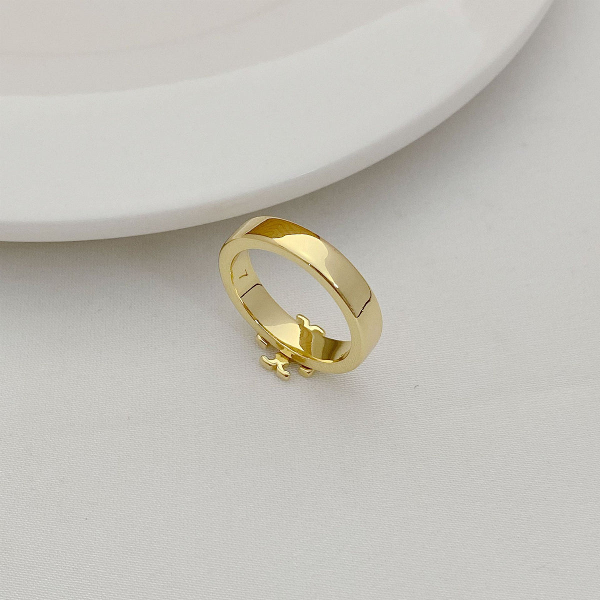 Gold-tone geometric letter-style ring, side view with raised emblem details