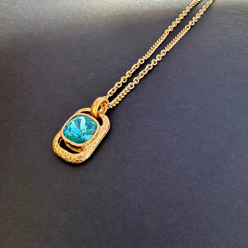 Gold-tone hammered square pendant necklace with faceted teal gemstone