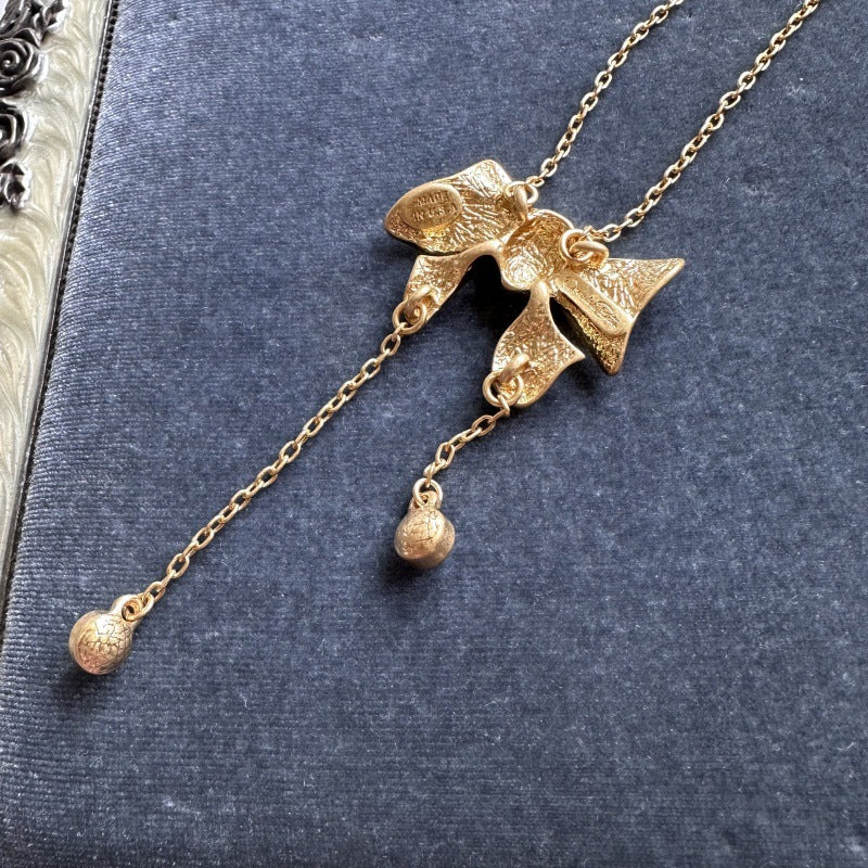 Gold-tone bow crystal tassel necklace close-up with three round crystal dangles