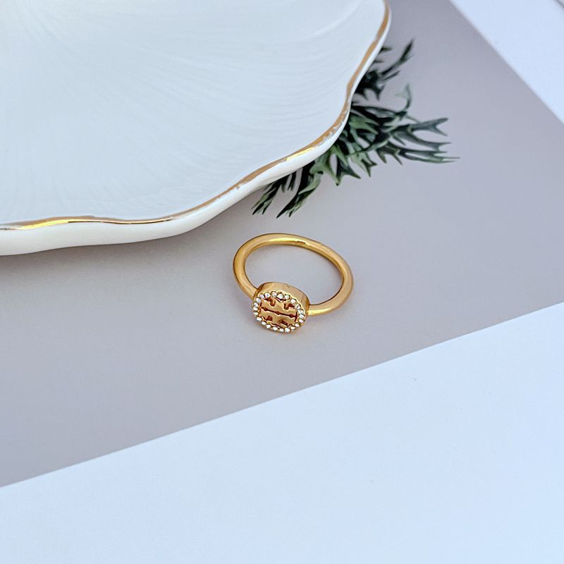 Gold-tone openwork logo ring on slim band, round center plate with pavé stones