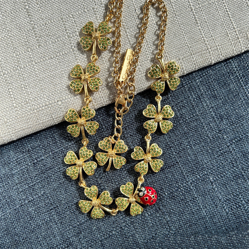 Green four-leaf clover necklace with red ladybug charm and layered gold chain