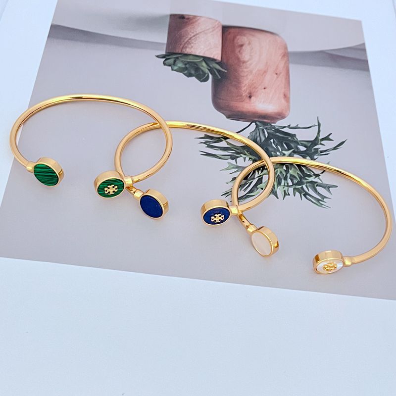 Gold-tone open bangle with round enamel discs in green, blue, and white.