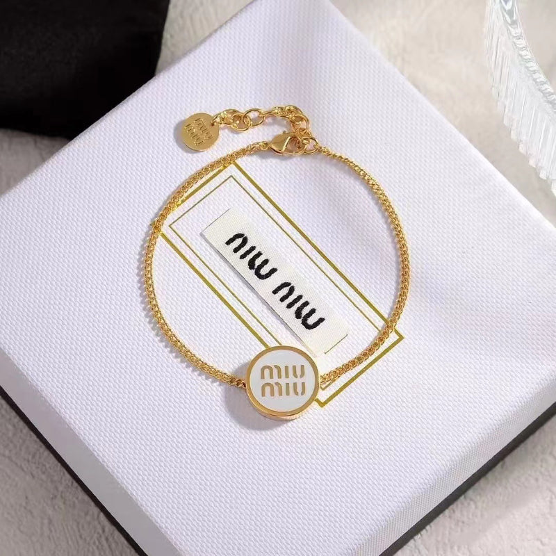 Close-up: round black enamel charm bracelet with gold chain and small logo tag.