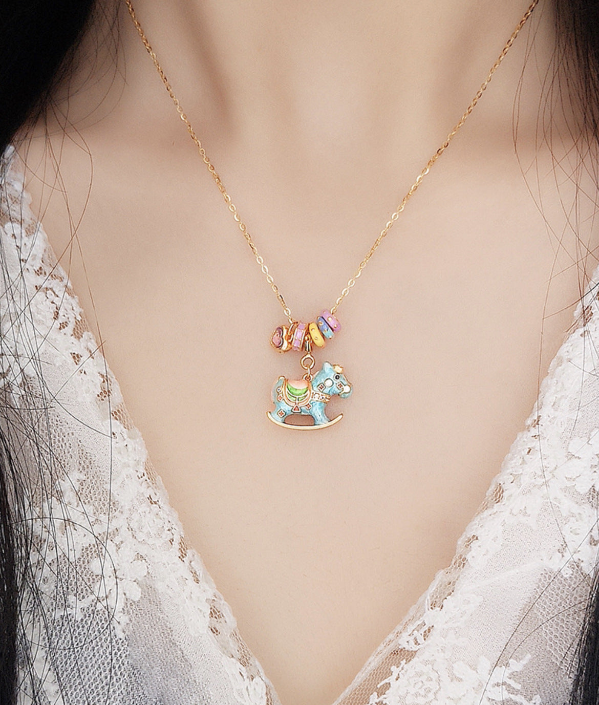 Enamel rocking horse necklace on neckline with gold chain, blue horse charm and cup pendant