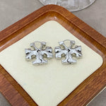 White gold 3D logo metal hoop earrings, sculpted floral emblem on display card