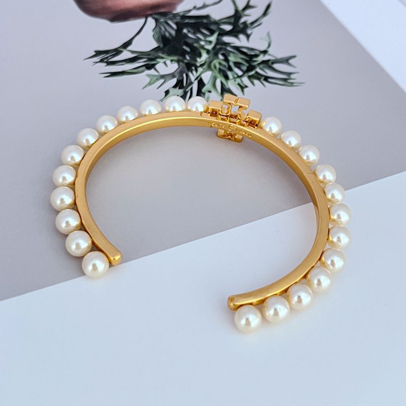 Gold-tone open bangle with white pearl trim and central logo bar