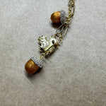Gold pendant necklace close-up with squirrel charm, two brown pinecone beads, sparkle stones