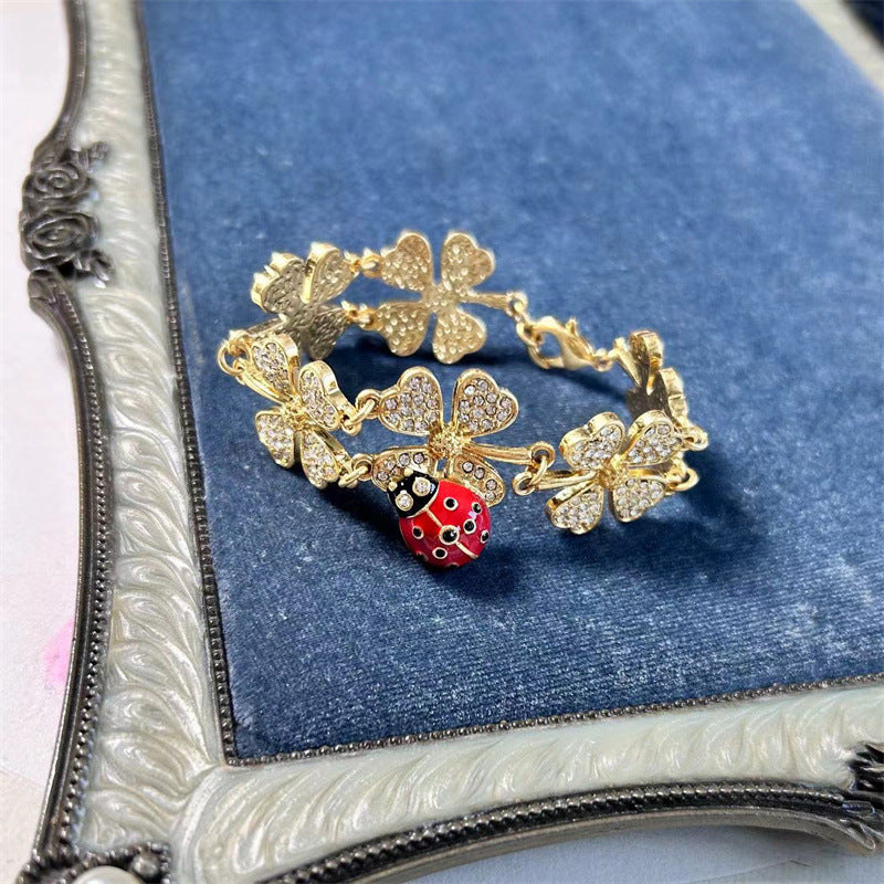 Gold-tone four-leaf clover charm bracelet with ladybug bead and hinged clasp