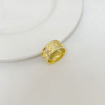 Gold metal letter band ring, close-up view with engraved vertical details
