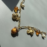 Gold-tone charm bracelet angled view with squirrel, acorn and pinecone charms and bead drops