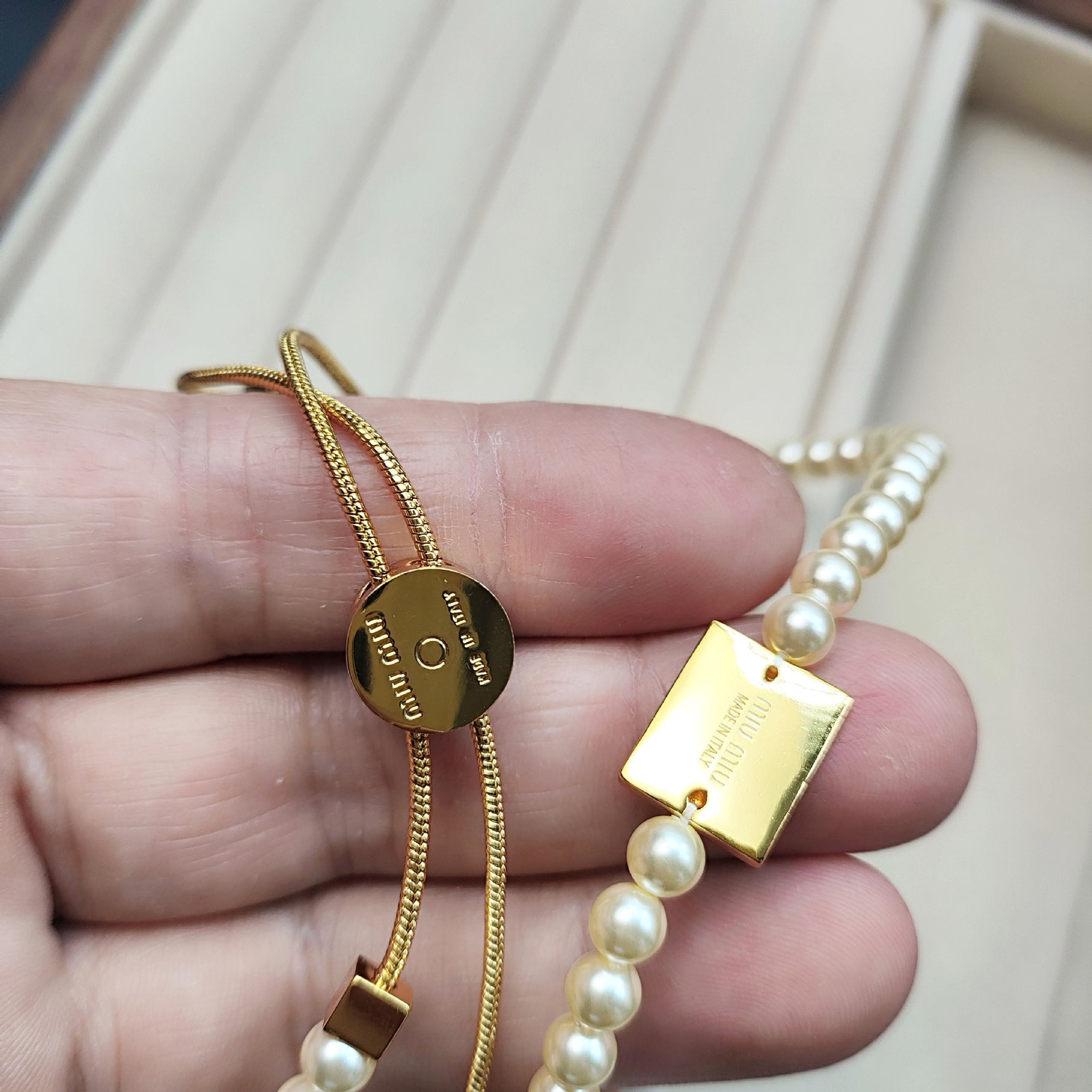 Gold round clasp with “Miu Miu” engraving and pearl bracelet-style necklace