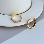 Gold hoop earrings with round logo cutout and crystal pavé detail