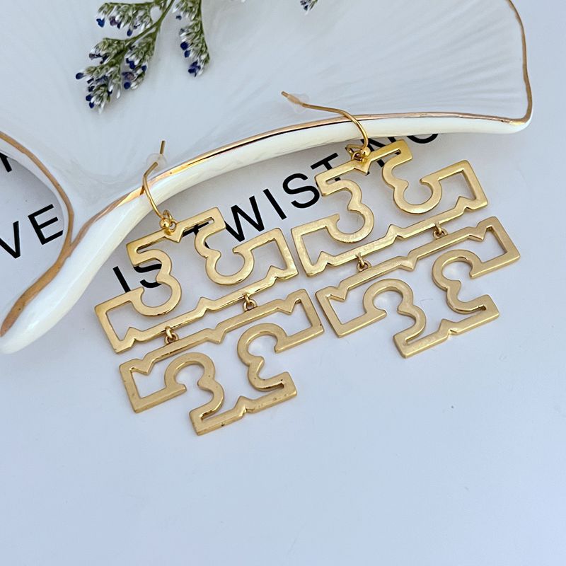 Gold metal openwork logo dangle earrings with hook backs, large geometric cutouts.