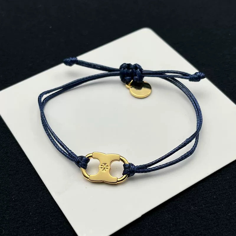 Dark blue woven adjustable drawstring bracelet with gold clover enamel charm and round tag