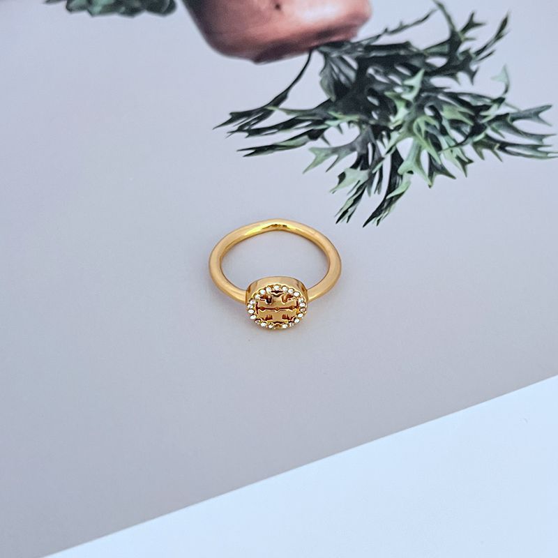 Gold-tone logo ring with round bezel and small clear stones on openwork plaque