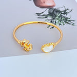 Gold open bangle with mother-of-pearl heart charm and heart clasp detail