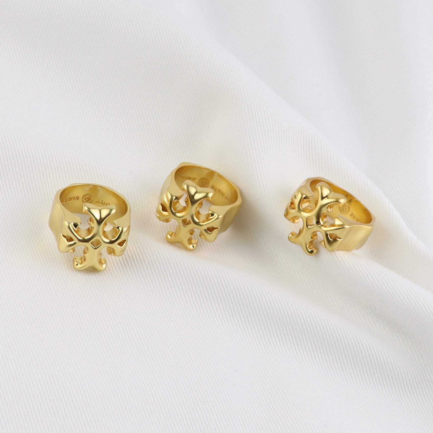Matte gold vintage ring with cutout logo motif, three angles on fabric