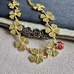 Close-up of gold four-leaf clover necklace with red ladybug and textured rose-like clasp