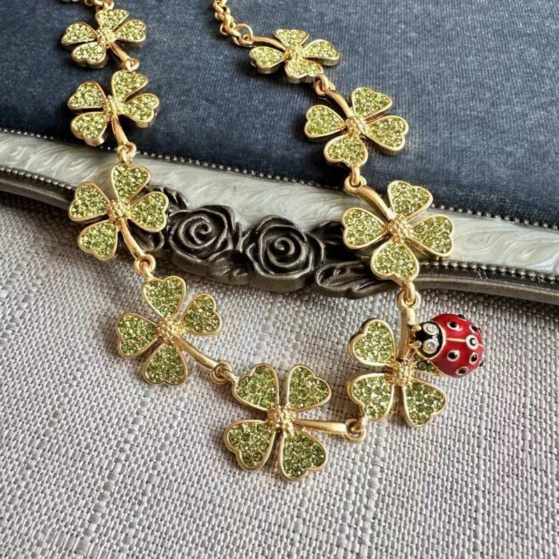 Close-up of gold four-leaf clover necklace with red ladybug and textured rose-like clasp