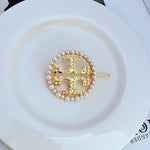 Gold metal hair clip, circular openwork logo with pearl bead border and flat pin