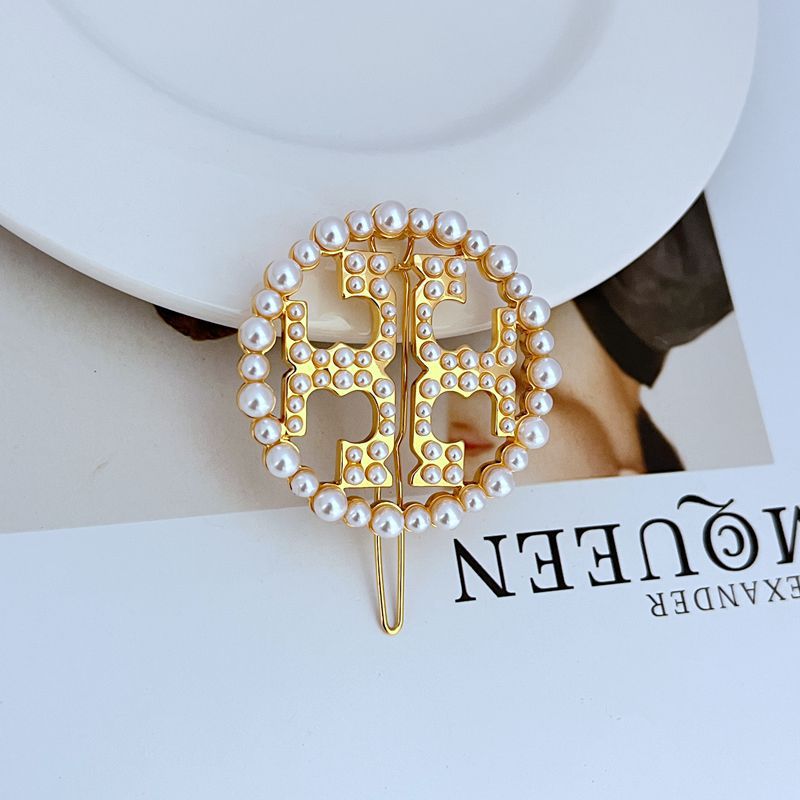 Gold circular openwork logo hair clip with pearl bead rim and curved prongs