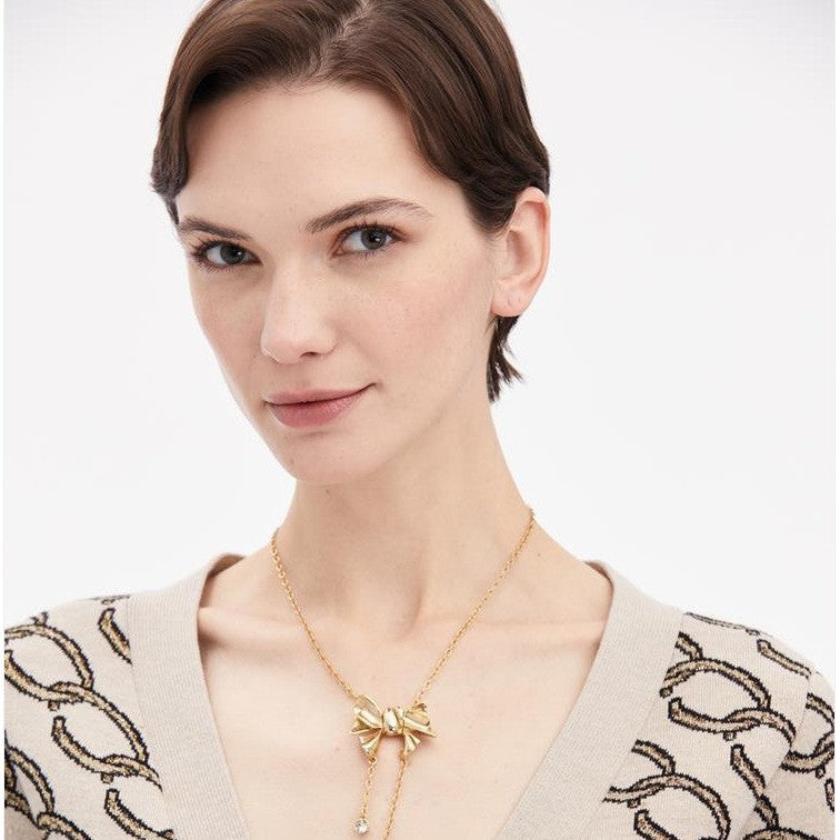 Gold bow necklace with dangling round crystal charms shown on a model
