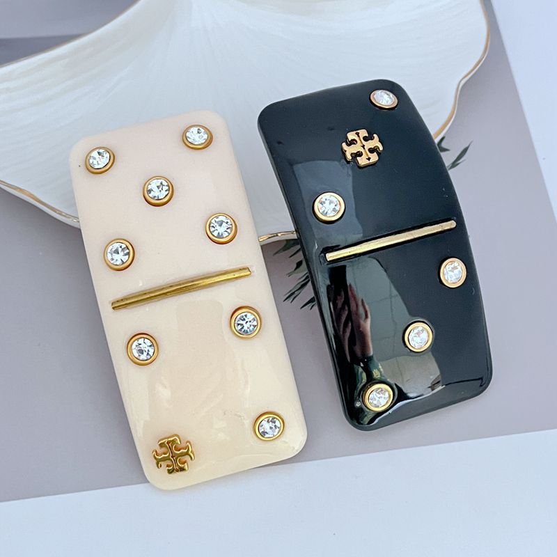 Black rectangular hair clip with gold logo, crystal studs, and gold bar