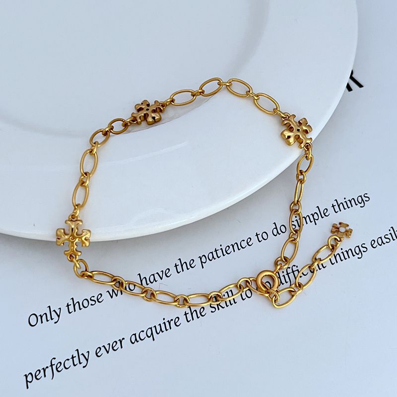 Interlocking logo chain bracelet with gold-tone clover charm accents and lobster clasp