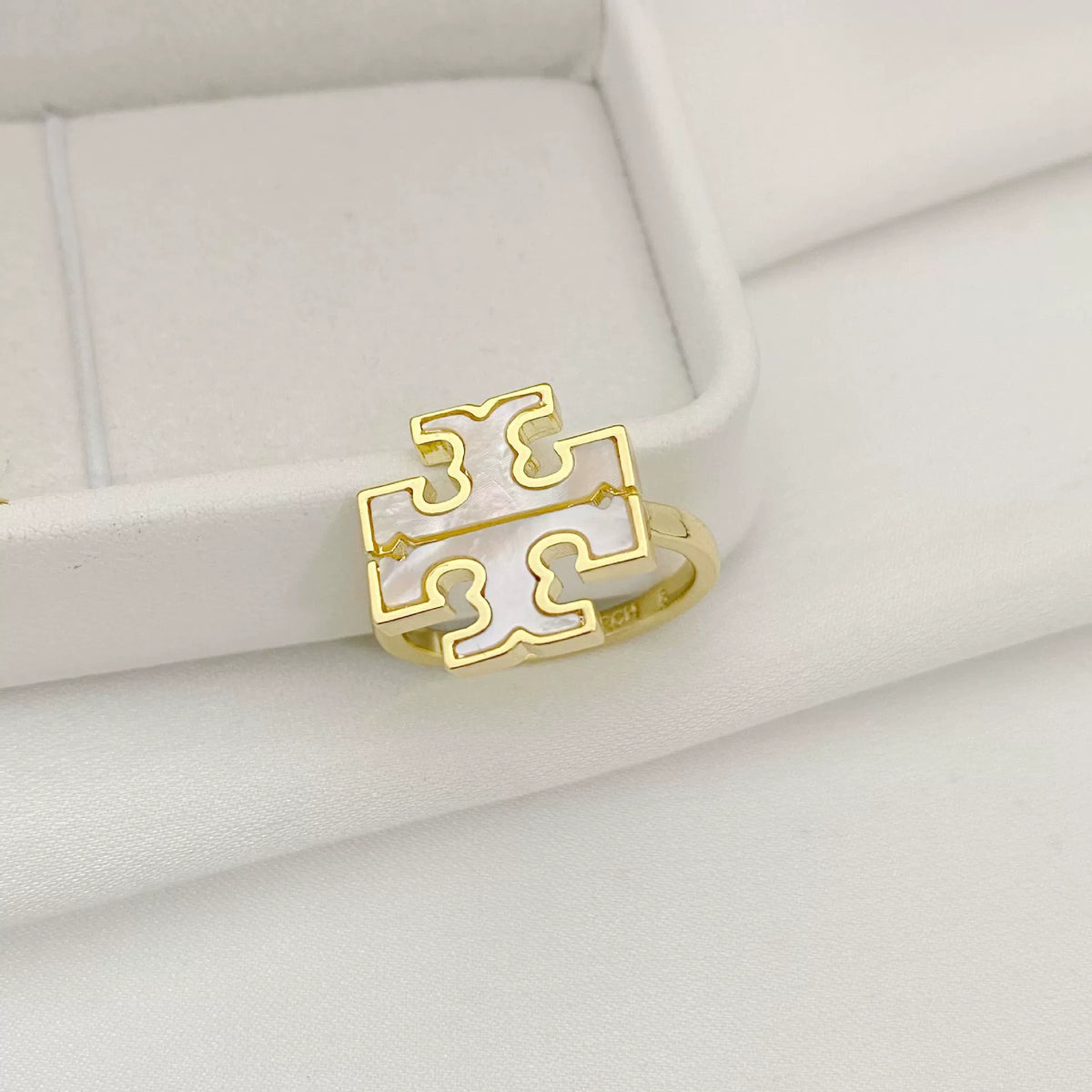 Gold logo ring set in a white jewelry box, featuring geometric cutouts