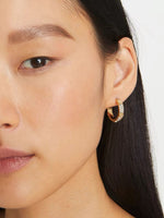 Gold hoop earrings with crystal pavé and logo detail, worn on model