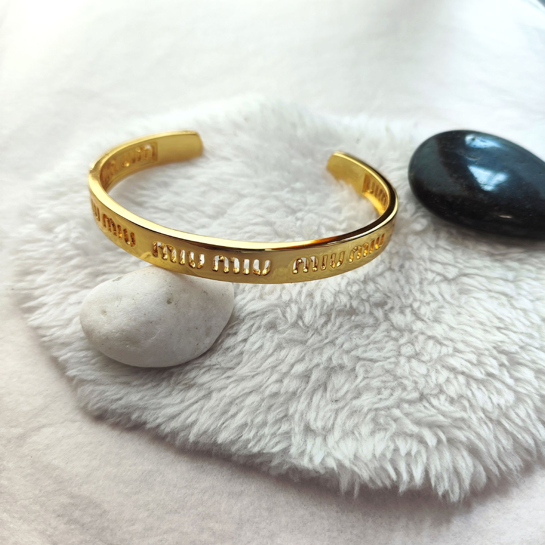 Gold openwork logo bangle on hand, wide cuff style with engraved lettering pattern